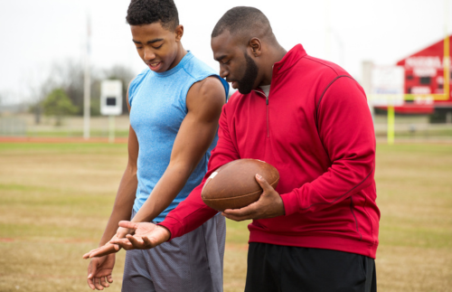 Male football coach showing a player how to hold the football