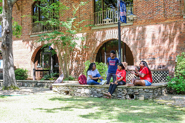 Three students collaborating at a laptop in a bright campus study area, focused and engaged, surrounded by books and modern furniture