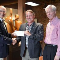 Three gentlemen smiling while one gives a check to to another 