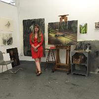 A student in a red dress standing next to her paintings 
