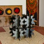 Dark geometric metal sculpture on table with Pasaquan art in background
