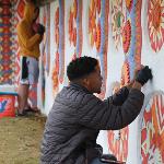 Person in a gray jacket painting a large outdoor mural.