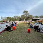 People painting a large outdoor mural on a grassy field.