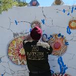 Artist in a black shirt painting colorful mandala designs on a white wall.