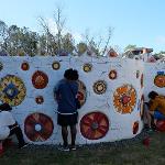 Two people working on a large white wall with colorful circular mural designs outdoors.