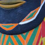Close-up detail of a painted totem face with chevron patterns in dark blue, orange, and green