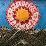 Painted sun medallion with yellow star center on a blue concrete wall