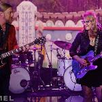 Live band performance on a colorfully decorated stage, with a guitarist playing an electric guitar under warm stage lighting.