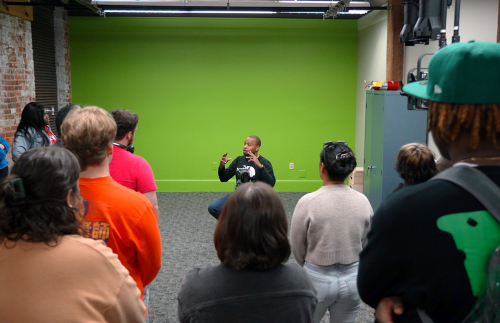 A man speaking with student in a room with a green screen behind him