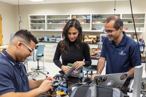 Two students and a professor working on a robotic device