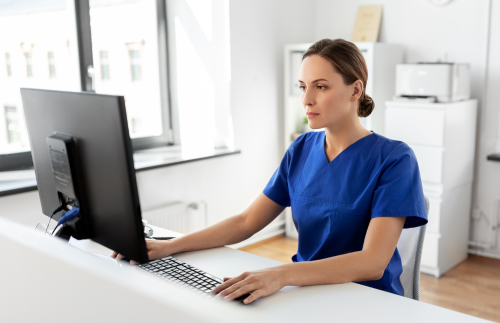 A nurse in scrubs at the counter on a computer