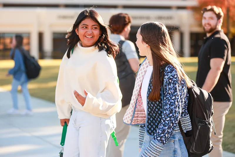 Two students smiling and talking outside a campus library building
