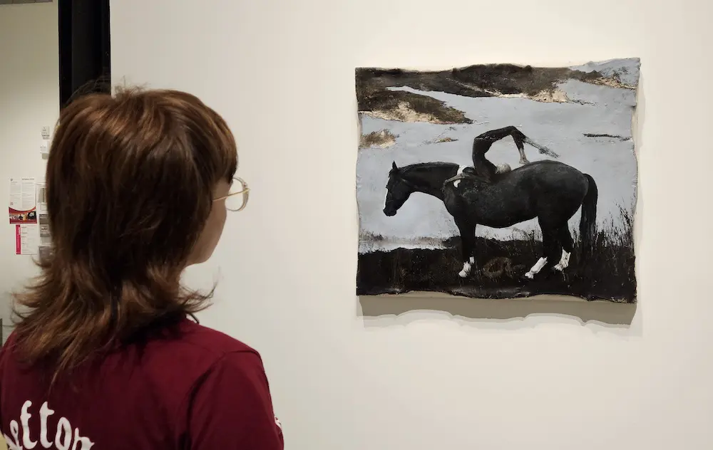 A woman looking at a painting of someone on a horse next to a body of water