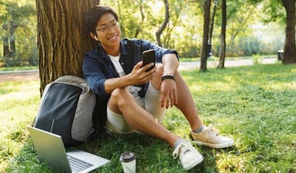 boy sitting in grass by a tree on his phone