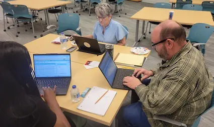 three people sitting at a desk with laptops