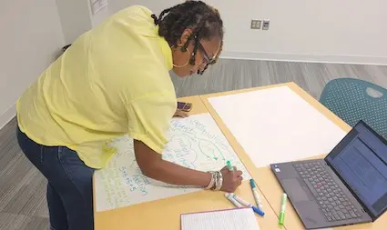 a woman at a desk with a laptop creating a poster
