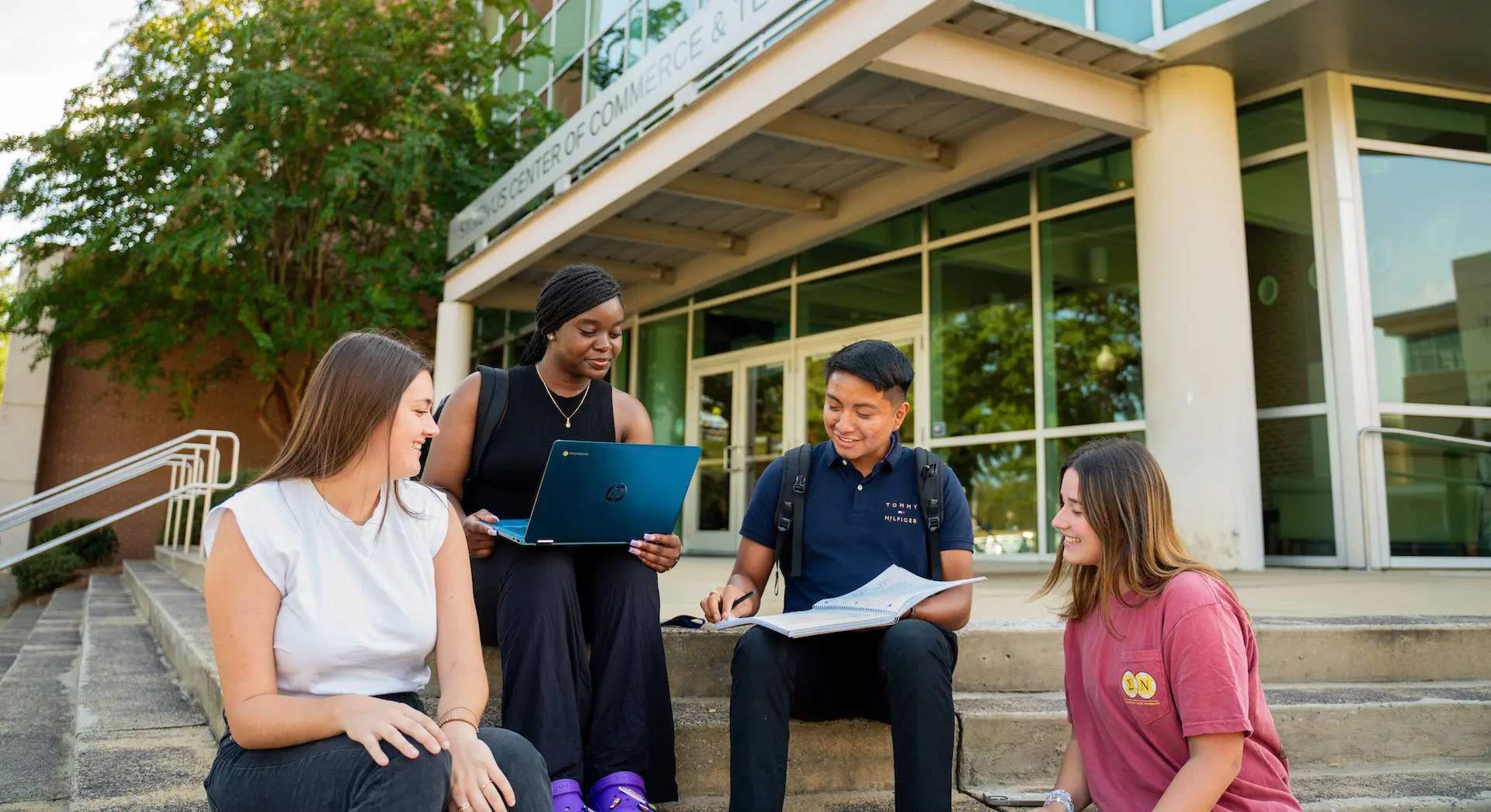 4 students sitting on the steps of the Synovus Technology building
