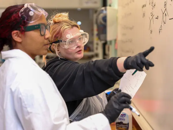 2 student working on chemistry formula at a whiteboard
