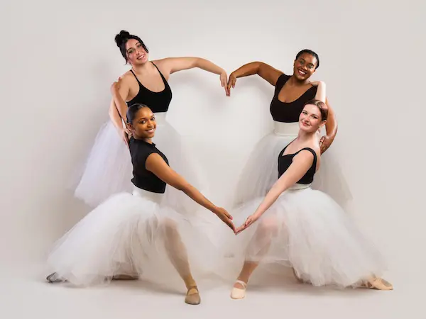 four female dance students in a circle connecting their arms to the shape of a heart