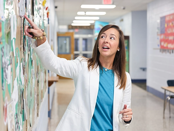 A teacher pointing at a picture on a wall for her class.