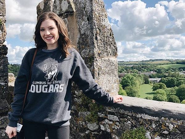 A student smiles as she stands by an old stone wall on a study abroad trip.