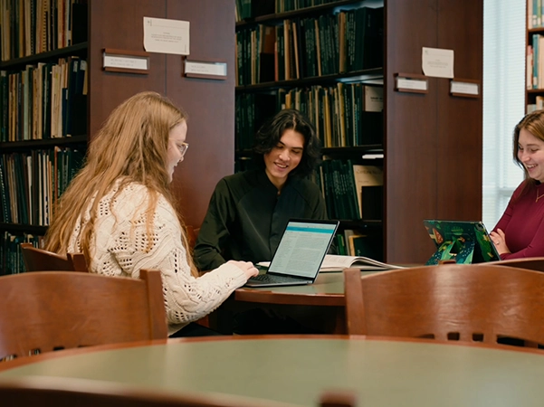 A group of students laughing and studying in a library.