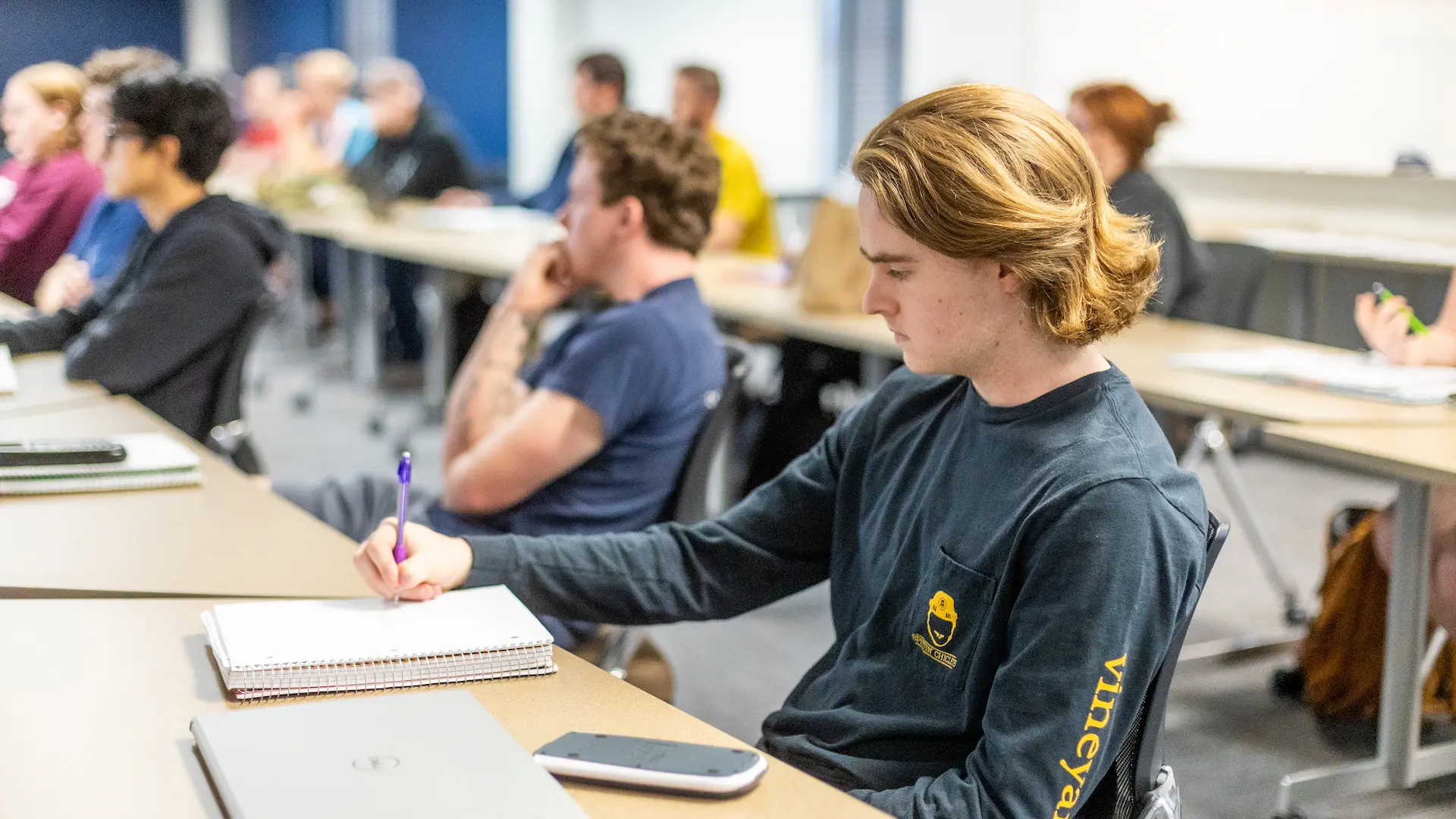 classroom of students sitting at their desks taking notes