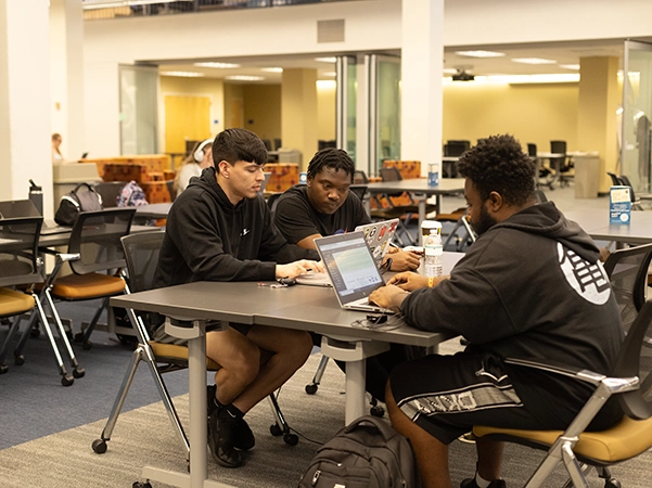 Three students studying on laptops at a table in the CSU library.