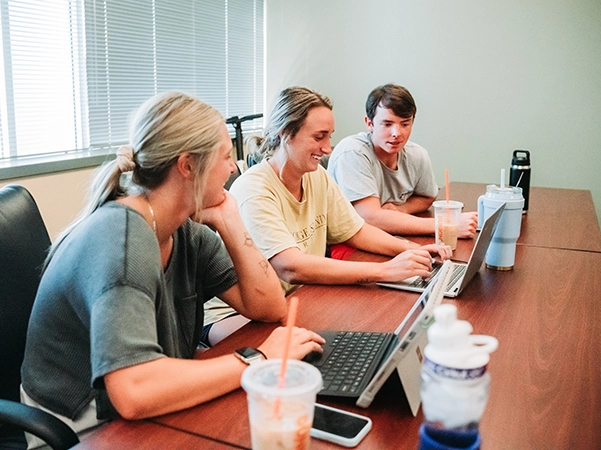 Three students work on a project together in a bright classroom.