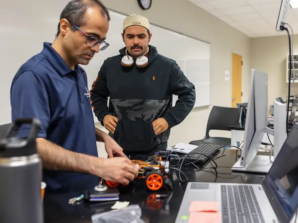 Robotics professor showing a student how to do something with a robot