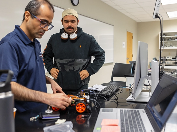 A student observing a professor work with robotic parts.