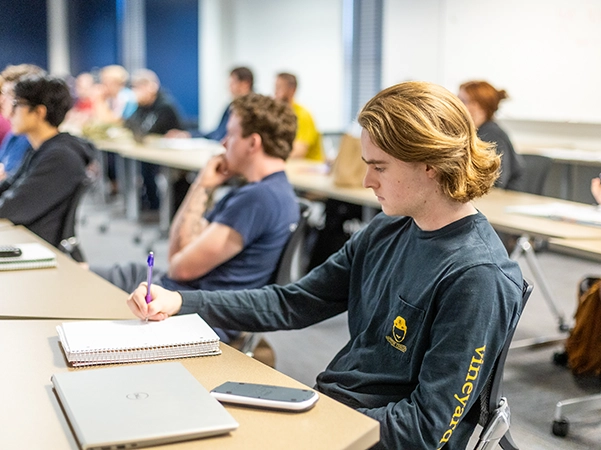 A student taking detailed notes in a bright classroom.