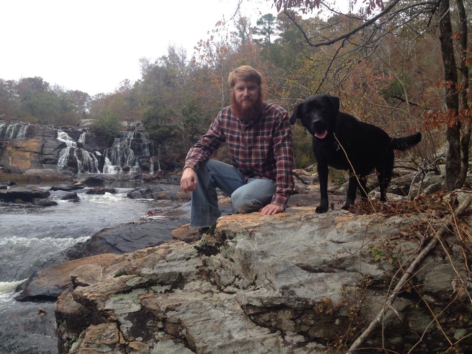 a male student and a black dog sitting next to a river