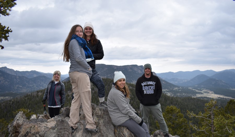 Four female students and one male student standing on a rock in front of mountains