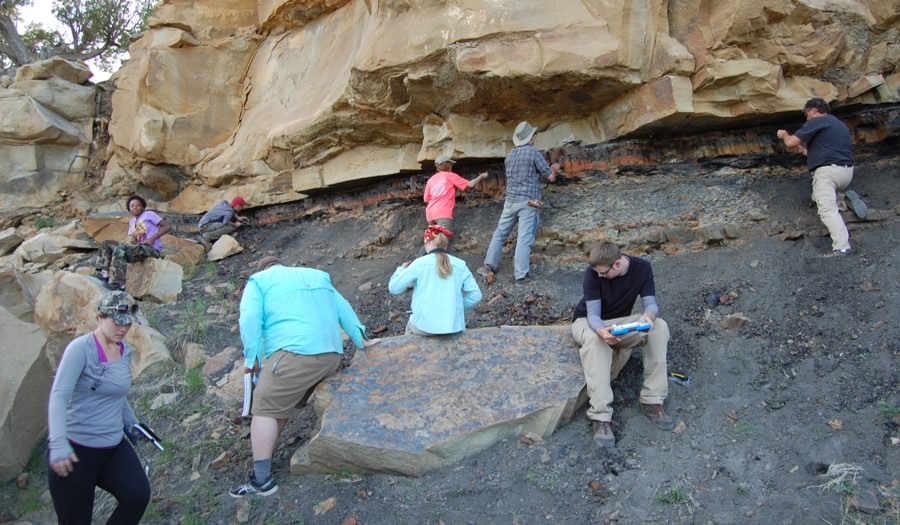 Several students standing below a cliff face