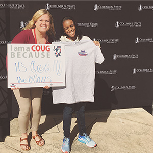 a female student and a woman standing and posing for a photo holding a sign