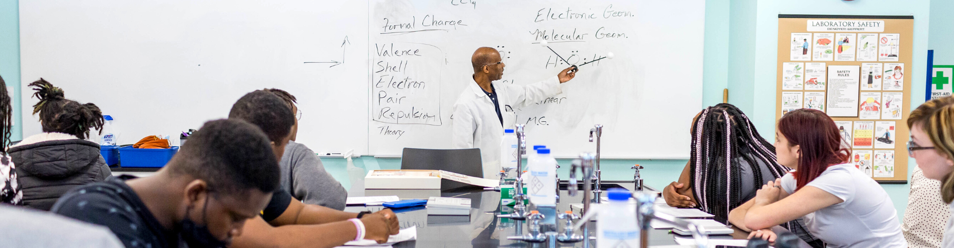 a male professor standing at a whiteboard talking to several students