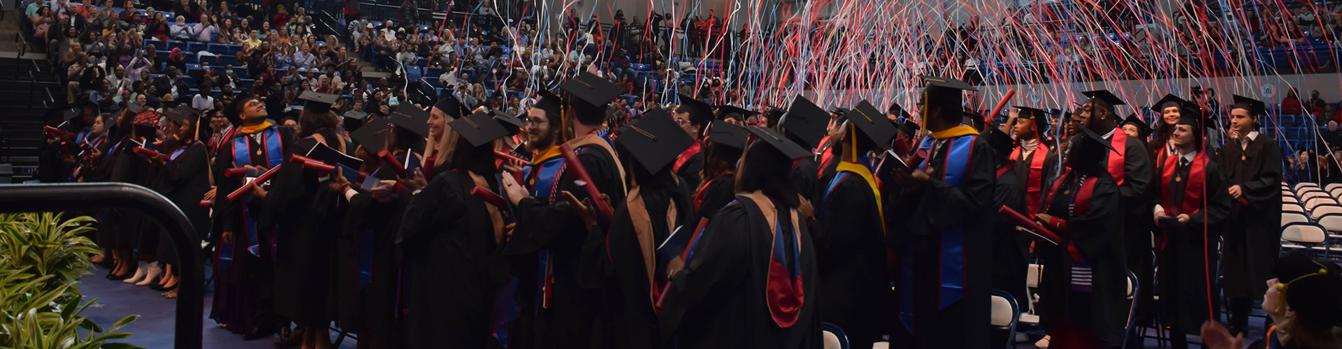 several students wearing graduation regalia with streamers in the background