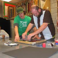 a professor assisting a student with a painting, another student looking on