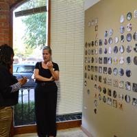 A wall with lots of small paintings and artworks neatly arranged, two females observing 