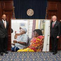 two men, both smiling and in suits, with a large painting between them 