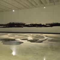 A large dark flat exhibit that is hanging from the ceiling, casting shadows on the floor 