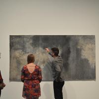 A man and two women discussing a large painting 