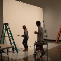 Two people next to ladders and a large white canvas 