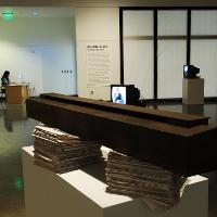 Art exhibit: a long brown boxy shape on two stacks of paper 