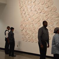 Onlookers next a large exhibit of many white circles/plates arranged to look like the state of Georgia 