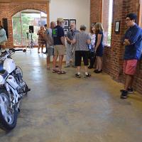 An onlooker next to an exhibit of a motorcycle, a group of other guests in the background 