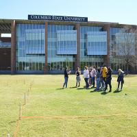 Students on a lawn, ropes and posts marking off designated areas 