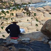 A person sitting on the rocks painting the river scene in front of them 
