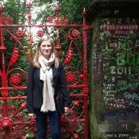 A student smiling outside Strawberry Fields and its bright red gate 